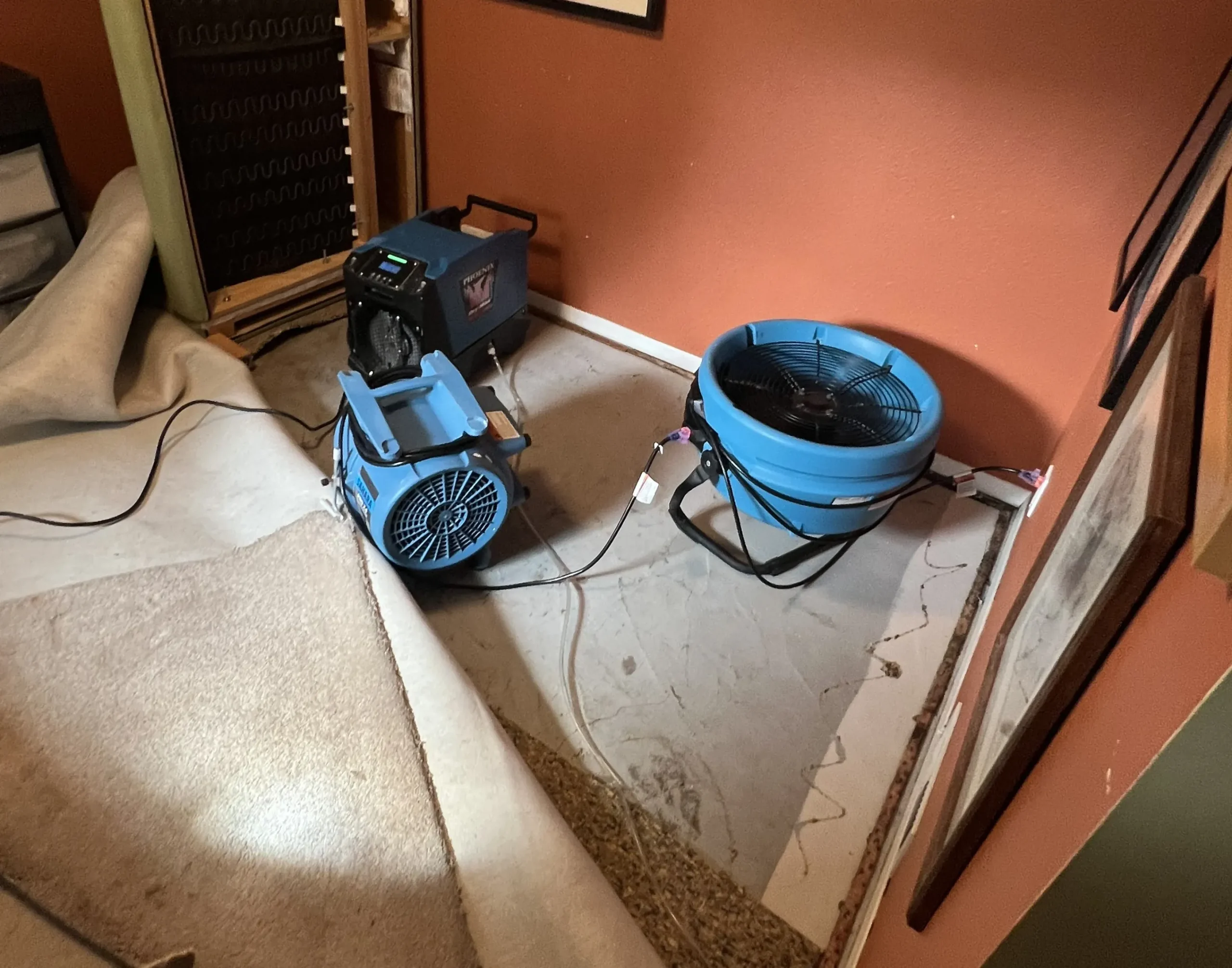 Air movers and a dehumidifier drying a room with exposed flooring